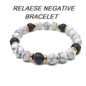 May include: A white and black beaded bracelet with gold accents. The bracelet features white marble-like beads and black lava rock beads.