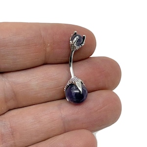May include: A silver body piercing with a purple gemstone on each end. The ends of the piercing are shaped like claws.