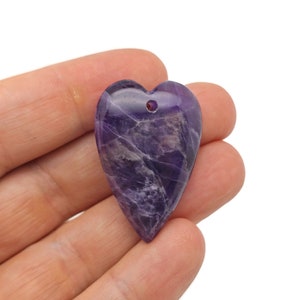 May include: A purple amethyst heart pendant with a drilled hole at the top. The heart is carved from a natural amethyst stone and has a unique, swirling pattern.