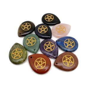 May include: A selection of teardrop-shaped stones in various colours, including black, green, and red. Each stone features a gold pentagram design. The stones are arranged on a white background.