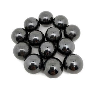 Puede incluir: Un conjunto de esferas brillantes, de color gris oscuro, dispuestas sobre un fondo blanco. Las esferas tienen una superficie reflectante, con reflejos visibles. Los objetos parecen estar hechos de un material liso y sólido.