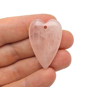 Puede incluir: Un colgante en forma de corazón de cuarzo rosa pálido con un pequeño agujero en la parte superior para enhebrar.