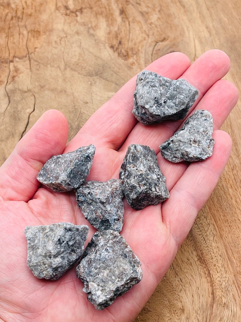 May include: A collection of seven small, rough, gray and black stones. The stones are in the palm of a hand.