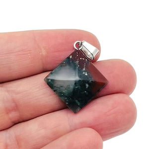 May include: A green, red and white gemstone pendant with a silver bail. The pendant is shaped like a square with rounded corners.