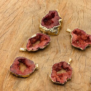 May include: Five red agate slices with gold-plated edges. Each slice has a natural, irregular shape and a hollow center. The slices are arranged on a wooden surface.