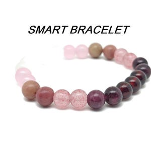 Könnte beinhalten: Ein rosa, rotes und braunes Perlenarmband mit dem Text "SMART BRACELET" darüber.