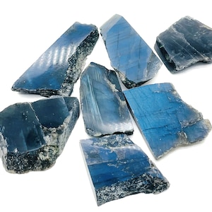 Puede incluir: Una colección de siete piezas de cristal de labradorita en bruto de color azul oscuro. Los cristales tienen una forma natural irregular y una superficie brillante e iridiscente.