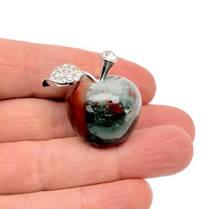 May include: A silver and green apple shaped paperweight with a rhinestone on the stem and rhinestones on the leaf.