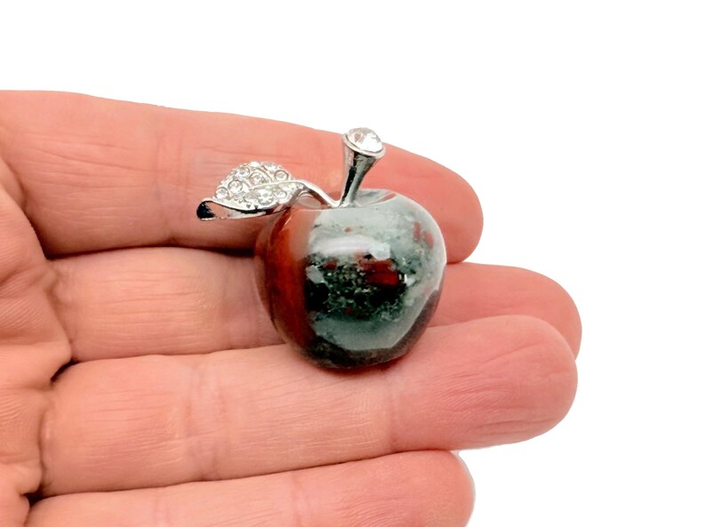May include: A silver and green apple shaped paperweight with a rhinestone on the stem and rhinestones on the leaf.