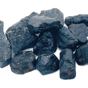 May include: A pile of black tourmaline rough stones. The stones are various shapes and sizes, with some having a slightly iridescent sheen.