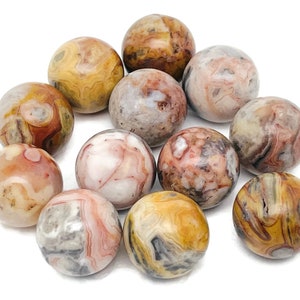May include: A collection of 12 smooth, round agate spheres with a variety of brown, white, and pink patterns. The spheres are arranged in a circle on a white background.