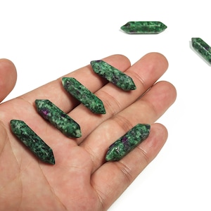 May include: Six green and purple gemstone points, also known as zoisite, are displayed on a hand. The points are approximately 2 inches long.