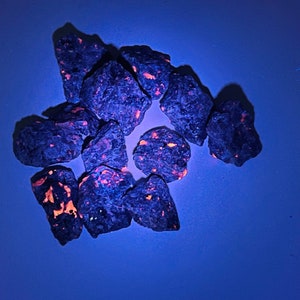 May include: A group of small, dark blue rocks with bright orange flecks. The rocks are arranged in a loose circle on a blue background.