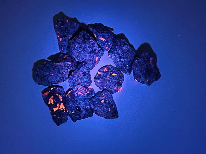 May include: A group of small, dark blue rocks with bright orange flecks. The rocks are arranged in a loose circle on a blue background.