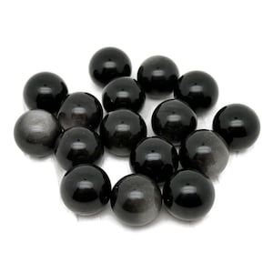 Könnte beinhalten: Eine Ansammlung polierter, kugelförmiger schwarzer Obsidiansteine. Einige Kugeln haben einen reflektierenden, metallischen Glanz, während andere tiefschwarz sind. Die Steine sind auf weißem Hintergrund angeordnet, wodurch ihre glänzenden Oberflächen hervorgehoben werden.