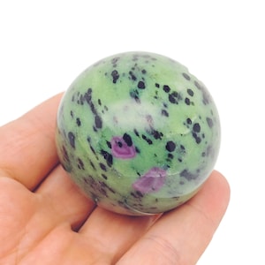 Könnte beinhalten: Grüne, schwarze und rosafarbene Edelsteinkugel. Die Kugel ist glatt und poliert.