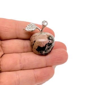 May include: A pink and black gemstone apple with a silver leaf and a clear rhinestone on top.