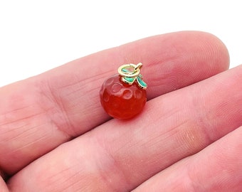 May include: A gold charm in the shape of a red orange with green leaves. The orange has a textured surface.