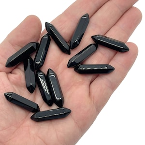 May include: A collection of black obsidian points, also known as arrowheads, in a hand. The points are smooth and polished, with a sharp tip.
