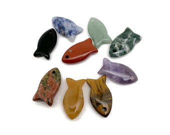 May include: A collection of gemstone fish figurines in various colors, including black, red, green, and purple. Each fish has a hole drilled near the top. The gemstones have unique patterns and textures.