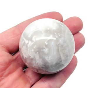 以下が含まれることがあります： 渦巻き模様の白いセレナイトの球体。球体は滑らかで磨かれています。