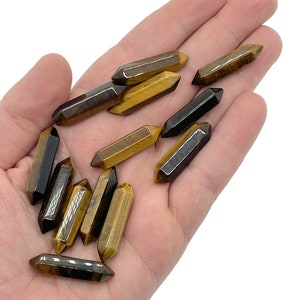 Pode incluir: Uma coleção de pontas de cristal de olho de tigre em vários tons de marrom e dourado. As pontas são lisas e polidas, com uma ponta pontiaguda e uma base plana.