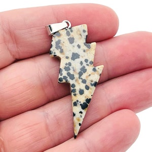 May include: A lightning bolt shaped pendant made of dalmatian jasper with black and white spots. The pendant has a silver bail.