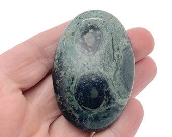 May include: A green and black polished stone with a swirling pattern. The stone is oval shaped and has a smooth, polished surface.