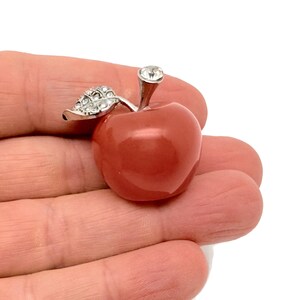 May include: A red gemstone apple with a silver stem and a clear rhinestone on top. The apple is about the size of a golf ball.