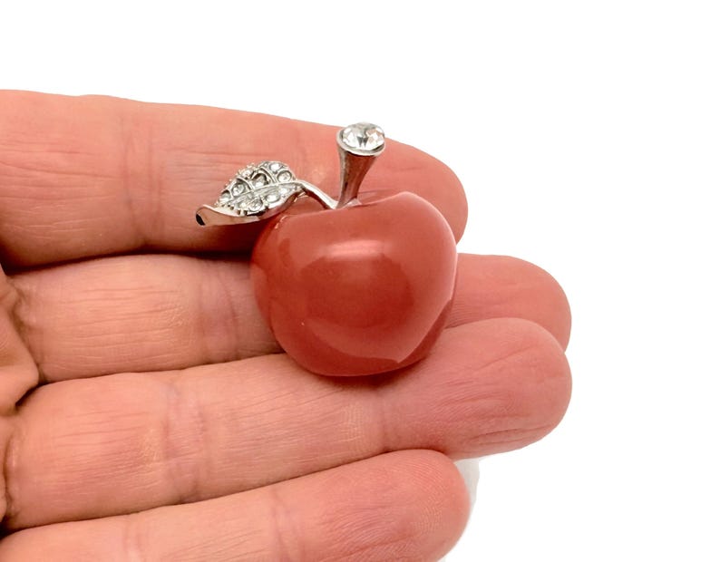 May include: A red gemstone apple with a silver stem and a clear rhinestone on top. The apple is about the size of a golf ball.