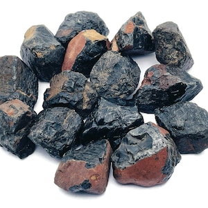 May include: A collection of black obsidian tumbled stones with a reddish-brown hue. The stones are rough and have a natural, unpolished finish.