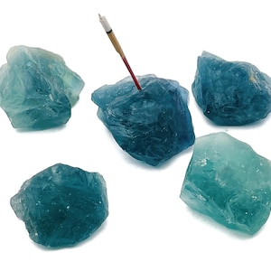 May include: Five teal blue fluorite crystals of varying sizes and shapes. One crystal has an incense stick inserted into it.