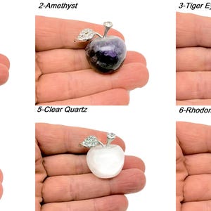 May include: Six different crystal apple pendants, each with a silver setting and a crystal stone. The stones are rose quartz, amethyst, tiger eye, obsidian, clear quartz, and rhodonite.