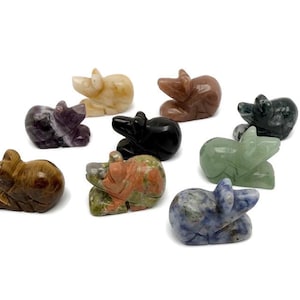 Pode incluir: Uma coleção de pequenas figuras de ursos de pedra esculpida em várias cores, incluindo castanho, preto, roxo e verde. Os ursos estão numa pose de descanso, com entalhes detalhados e superfícies polidas. As figuras são exibidas sobre um fundo branco.