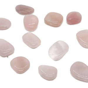 Könnte beinhalten: Eine Sammlung von 12 rosa Rosenquarz-Trommelsteinen. Die Steine sind glatt und poliert und haben eine natürliche, unregelmäßige Form.
