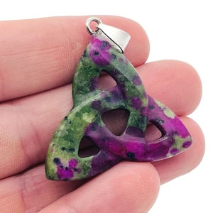 May include: A green and purple gemstone pendant in the shape of a Celtic knot. The pendant is made of a polished stone with a silver bail.
