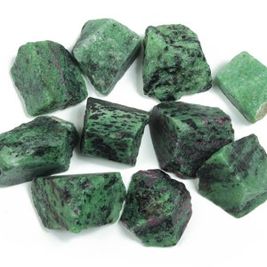 Puede incluir: Una colección de diez piedras preciosas de zultanita en bruto de color verde, negro y rosa. Las piedras son de varios tamaños y formas.