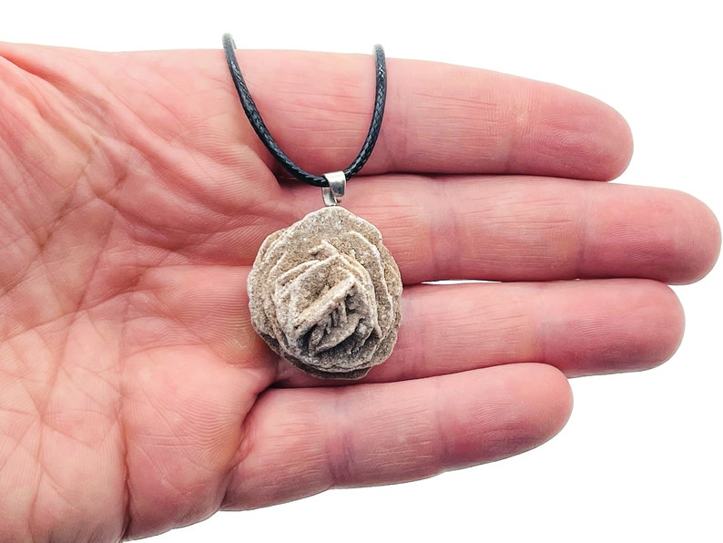 May include: A delicate rose quartz pendant necklace with a natural rose quartz stone. The pendant is on a black cord necklace.
