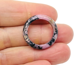 Pode incluir: Um anel rosa e preto feito de pedra de rodocrosita polida. O anel é uma banda simples com uma superfície lisa e arredondada.