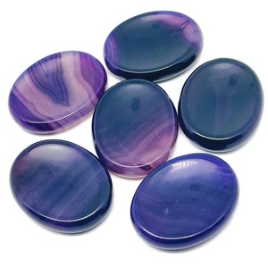 May include: Six purple and pink agate palm stones. The stones are oval shaped and have a smooth, polished finish.