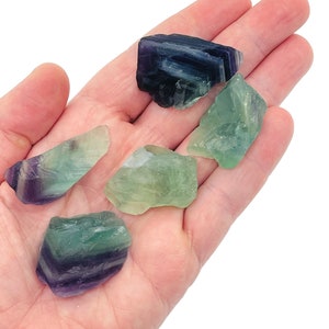 May include: Five green and purple fluorite crystals in various shapes and sizes, held in a hand.