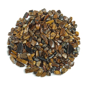 May include: A close-up of a pile of tiger's eye gemstone chips. The chips are a mix of brown, gold, and black colors. They are irregularly shaped and have a smooth, polished finish.