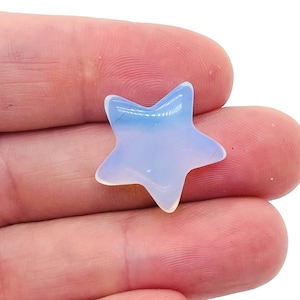 Puede incluir: Una pieza de ópalo de color azul pálido en forma de estrella, sostenida en una mano.