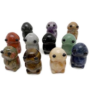 May include: A collection of eleven small, carved stone figurines in various colors and patterns. The figurines have a rounded body shape with small, black, round eyes. The stones include red, green, black, and brown.