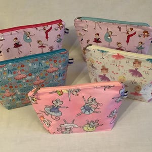 May include: Five different pink and blue zippered pouches with various ballerina and mouse designs. The pouches are made of fabric and have a zipper closure.