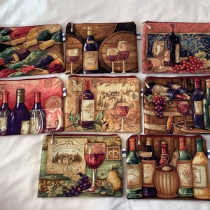 May include: Set of ten zippered pouches with various wine-themed designs. Each pouch features a different design with wine bottles, grapes, and glasses. The pouches are made of a fabric material with a red zipper.