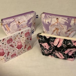 May include: Four different zippered pouches with various ballet-themed prints. The pouches are made of a soft, fabric material and have a zipper closure. The prints include a ballerina in a white tutu, pink ballet shoes, and a pink tutu with stars.
