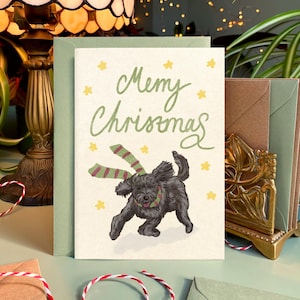 May include: A Christmas card with the words "Merry Chrismas" in green script, featuring a black dog wearing a green and red striped scarf. The card is on a light green background with yellow star accents.