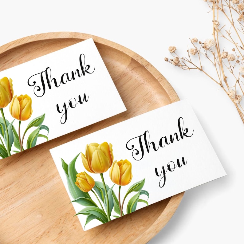 Puede incluir: Dos tarjetas blancas con el texto "Gracias" en letra cursiva negra. Una tarjeta presenta un ramo de tulipes amarillas con hojas verdes.