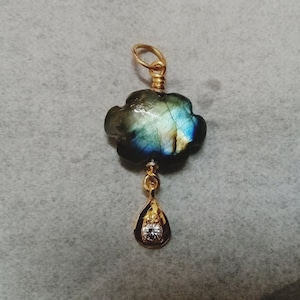 May include: A gold pendant featuring a blue and green labradorite gemstone in a flower shape with a small clear crystal dangling below.